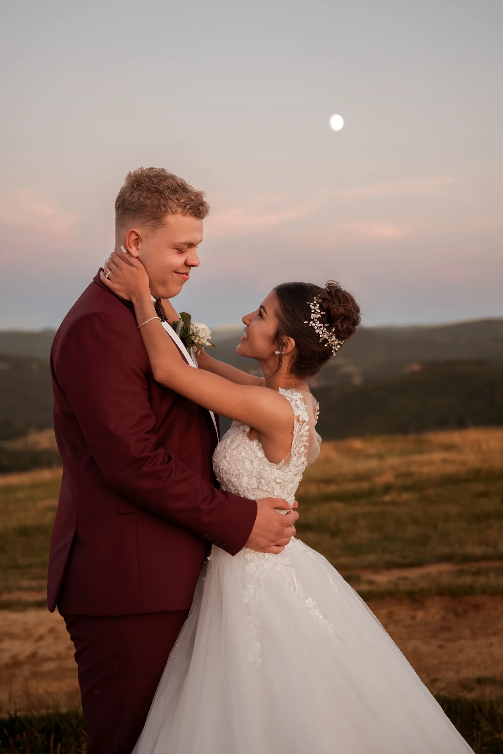Novomanželé v objetí za soumraku, na obloze vychází měsíc